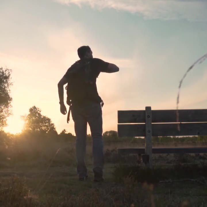 Ein Wanderer mit Rucksack bei Sonnenuntergang neben einer Bank